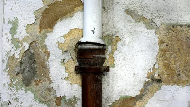 Rusted pipe through a wall with peeling paint and water stains