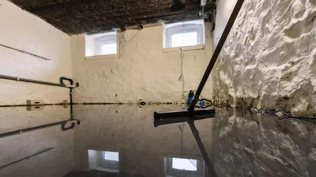 Flooded unfinished basement with a squeegee on the floor