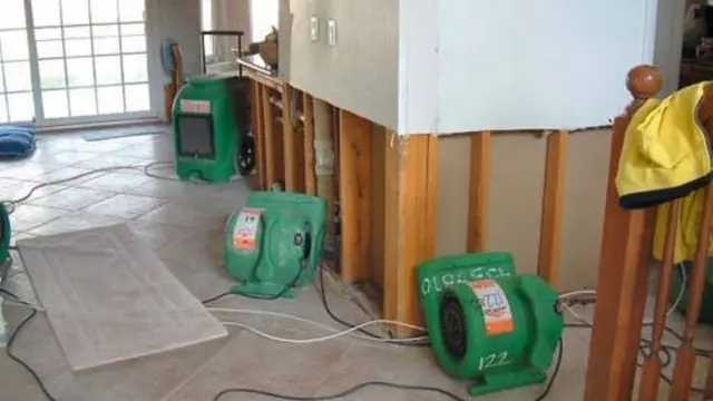 Air movers and a dehumidifier running beside opened wall framing