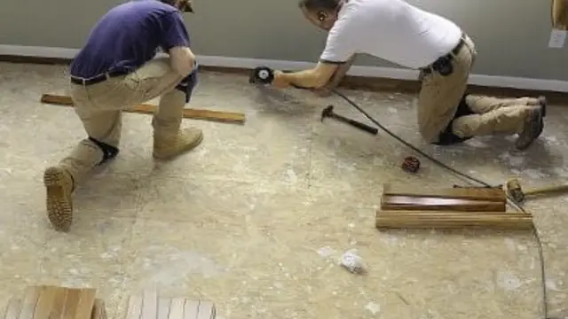 Two workers kneeling on a subfloor to install new flooring