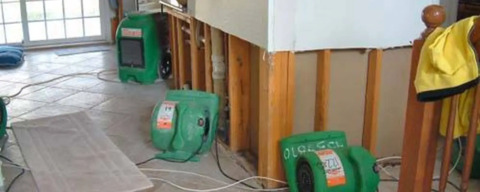 Air movers and a dehumidifier running beside opened wall framing